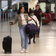 Passengers at the San Francisco International airport walk with rolling bags. Some are wearing masks, and others are not.